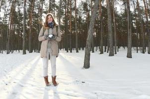 een jong en blij Kaukasisch meisje in een bruin jas houdt een sneeuwbal in een met sneeuw bedekt Woud in winter. vissenoog foto