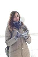 een jong en blij Kaukasisch meisje in een bruin jas houdt een sneeuwbal in de achtergrond van een horizon lijn tussen de lucht en een bevroren meer in winter foto