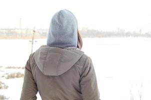 een jong Kaukasisch meisje in een bruin jas staren in de afstand Aan de horizon lijn tussen de lucht en de bevroren meer in winter foto