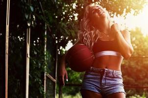 jong blond meisje met oranje basketbal poseren buitenshuis foto