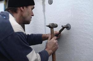 een ouderen werkman klompen een deuvel in een plastic paraplu monteren in een piepschuim muur. de werkwijze van vaststelling uitgebreid polystyreen platen. opwarming van de facade van de gebouw foto