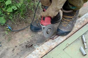 elektrisch wiel slijpen Aan staal structuur buitenshuis. oud handleiding arbeider in beschermend handschoenen snijdend metaal deur met Slijper foto