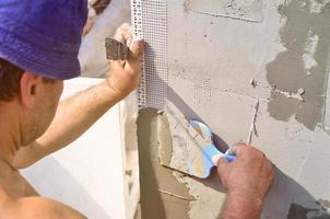 vijftig jaren oud handleiding arbeider met muur bepleistering gereedschap renoveren huis. stukadoor renoveren muren en hoeken met spatel en gips. muur puree installatie. bouw afwerking werken foto