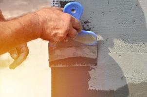 handen van een oud handleiding arbeider met muur bepleistering gereedschap renoveren huis. stukadoor renoveren buitenshuis muren en hoeken met spatel en gips. muur isolatie. bouw afwerking werken foto