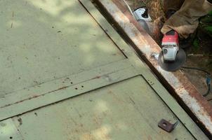 elektrisch wiel slijpen Aan staal structuur buitenshuis. oud handleiding arbeider in beschermend handschoenen snijdend metaal deur met Slijper foto