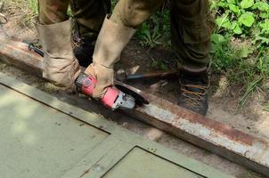 elektrisch wiel slijpen Aan staal structuur buitenshuis. oud handleiding arbeider in beschermend handschoenen snijdend metaal deur met Slijper foto