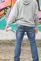 een jong graffiti artiest in een grijs capuchon looks Bij de muur met foto