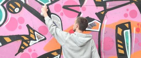 een jong vent in een grijs capuchon verven graffiti in roze en groen c foto