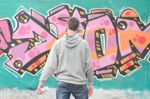 een jong graffiti artiest in een grijs capuchon looks Bij de muur met foto