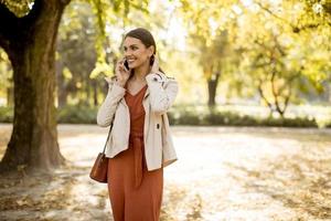 gelukkige jonge vrouw die mobiele telefoon gebruikt in het herfstpark