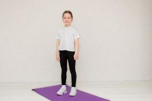 schattig weinig meisje in sportkleding staat Aan een gymnastiek- mat klaar voor opleiding foto