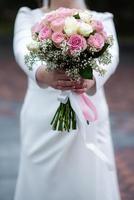 de bruid in een wit bruiloft jurk is Holding een boeket van wit bloemen - pioenrozen, rozen. bruiloft. bruid en bruidegom. delicaat Welkom boeket. mooi decoratie van bruiloften met bladeren foto