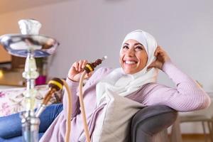 moslim vrouw roken shisha Bij huis. moslim jong vrouw genieten van terwijl roken nargiel. Arabisch meisje roken hookah foto