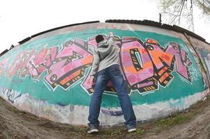 een jong vent in een grijs capuchon verven graffiti in roze en groen c foto