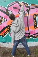 een jong vent in een grijs capuchon verven graffiti in roze en groen c foto