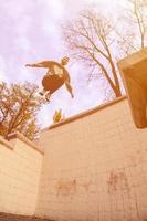 een jong vent presteert een springen door de ruimte tussen de beton borstweringen. de atleet praktijken parkour, opleiding in straat conditie. de concept van sport- subculturen tussen jeugd foto