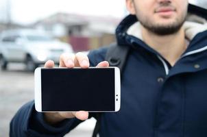 een jong vent demonstreert een smartphone Scherm Aan de achtergrond foto