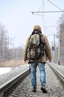 een Mens met een groot rugzak gaat verder Aan de spoorweg bijhouden duri foto