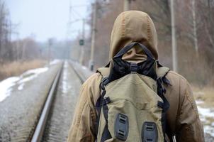 een Mens met een groot rugzak gaat verder Aan de spoorweg bijhouden duri foto