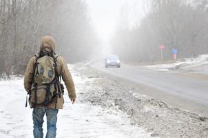 een Mens met een groot rugzak wandelingen langs een buitenwijk asfalt weg foto