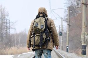 een Mens met een groot rugzak gaat verder Aan de spoorweg bijhouden duri foto