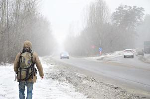 een Mens met een groot rugzak wandelingen langs een buitenwijk asfalt weg foto