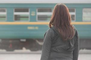 een jong roodharig meisje is staand Aan de spoorweg platform en aan het kijken de vertrek trein. de vrouw was laat voor haar trein. terug visie foto