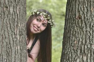 een Woud afbeelding van een mooi jong brunette van Europese uiterlijk met donker bruin ogen en groot lippen. Aan de meisjes hoofd is vervelend een bloemen lauwerkrans, Aan haar voorhoofd glimmend decoraties foto