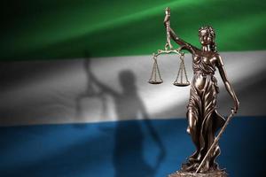 Sierra Leone vlag met standbeeld van dame gerechtigheid en gerechtelijk balans in donker kamer. concept van oordeel en straf foto