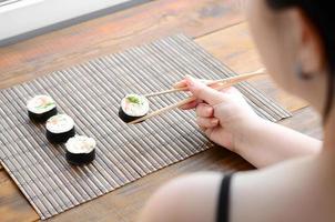 brunette meisje met eetstokjes houdt een sushi rollen Aan een bamboe rietje naaien mat achtergrond. traditioneel Aziatisch voedsel foto