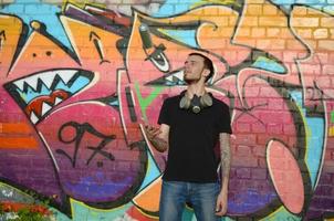 jong graffiti artiest met gas- masker Aan zijn nek Gooi zijn verstuiven kan tegen kleurrijk roze graffiti Aan steen muur. straat kunst en hedendaags schilderij werkwijze foto