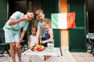 gelukkig vier kinderen tegen Italiaans vlag vieren republiek dag van Italië en eten vruchten. foto