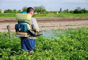 een boer met een de nevel vernevelaar sproeier sprays fungicide en pesticide Aan aardappel struiken. bescherming van gecultiveerd planten van insecten en schimmel infecties. effectief Bijsnijden bescherming, milieu gevolg foto