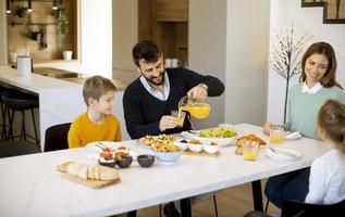 jong gelukkig familie pratend terwijl hebben ontbijt Bij dining tafel foto