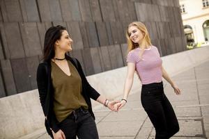 twee jong Dames wandelen Aan de straat en Holding handen foto