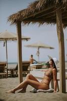 jong vrouw in bikini zittend Aan de strand Bij zomer dag foto