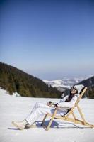 jong vrouw zittend Bij dek stoel Aan ski bijhouden Bij de besneeuwd berg foto