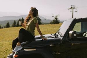 jonge vrouw ontspannen op de motorkap van een terreinvoertuig op het platteland foto