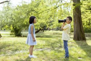 weinig Aziatisch jongen acteren Leuk vinden een professioneel fotograaf terwijl nemen foto's van zijn weinig zus foto