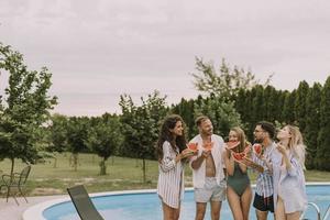 jong mensen staand door de zwemmen zwembad en aan het eten watermellon in de huis achtertuin foto