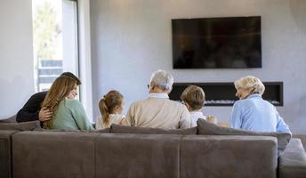 multi generatie familie zittend samen Aan de sofa Bij huis en aan het kijken TV foto