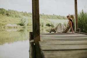 ontspannende jonge vrouw op houten pier aan het meer foto