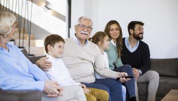 multi generatie familie zittend samen Aan de sofa Bij huis en aan het kijken TV foto