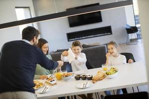 jong gelukkig familie pratend terwijl hebben ontbijt Bij dining tafel foto
