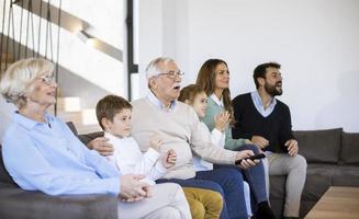 multi generatie familie zittend samen Aan de sofa Bij huis en aan het kijken TV foto