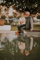 opa uitgeven tijd met zijn kleindochter door klein water zwembad in park Aan herfst dag foto