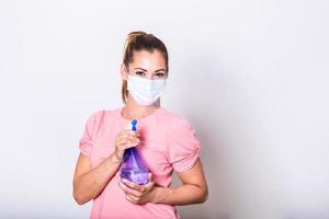 vrouw met beschermend gelaats masker en ontsmettingsmiddel verstuiven fles . ze sprenkeling ontsmettingsmiddel en schoonmaak de glas. blijven veilig. foto