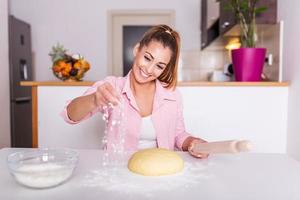 gelukkig vrouw kneden deeg Bij huis keuken. jong vrolijk vrouw maken brood, huisvrouw meisje Koken voedsel in de keuken foto