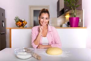 mooi jong vrouw op zoek Bij camera en glimlachen terwijl bakken in keuken Bij huis. glimlachen jong huisvrouw maken deeg foto