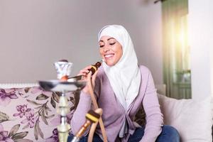 moslim vrouw roken shisha Bij huis. moslim jong vrouw genieten van terwijl roken nargiel. Arabisch meisje roken hookah foto